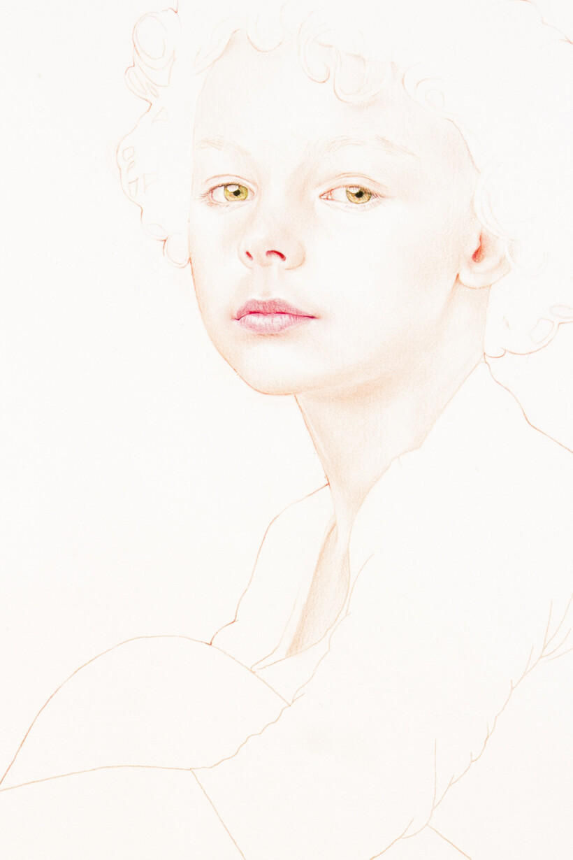 Primer plano del rostro de un niño con rizos y ojos claros, sentado en un fondo blanco.