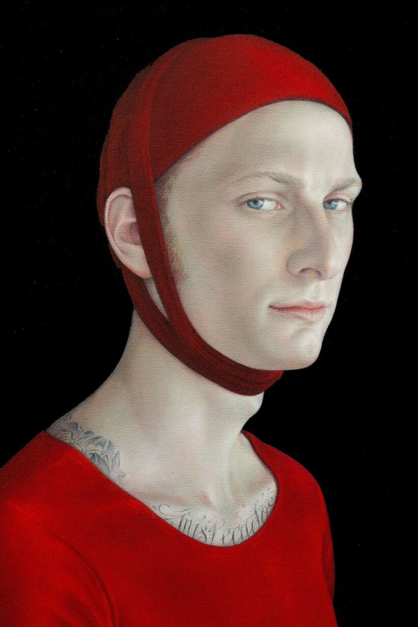 Retrato de un joven con gorro de tela rojo, camiseta del mismo color y tatuajes en el cuello.