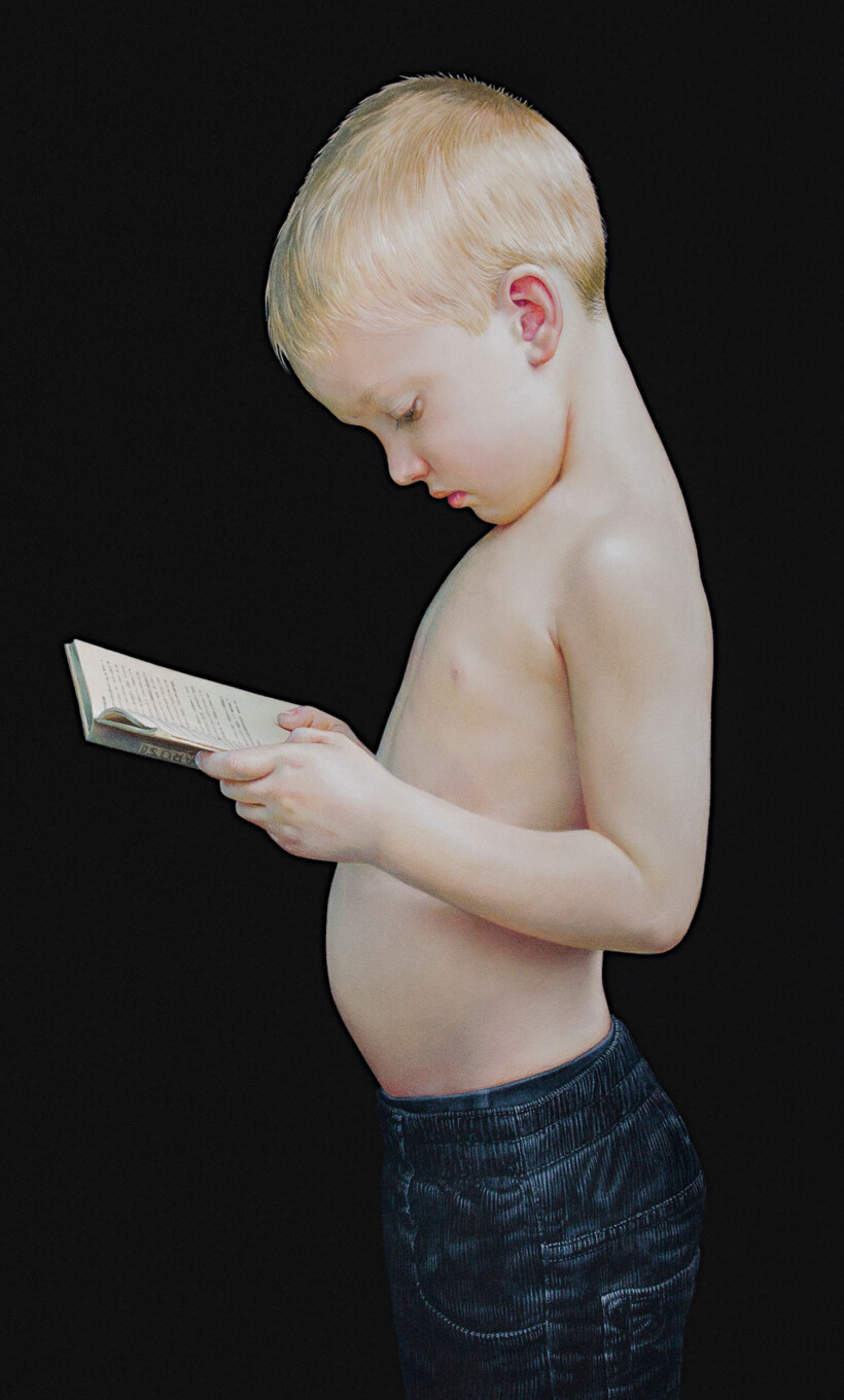 Retrato de un niño rubio sin camisa, de perfil, leyendo un libro con concentración.
